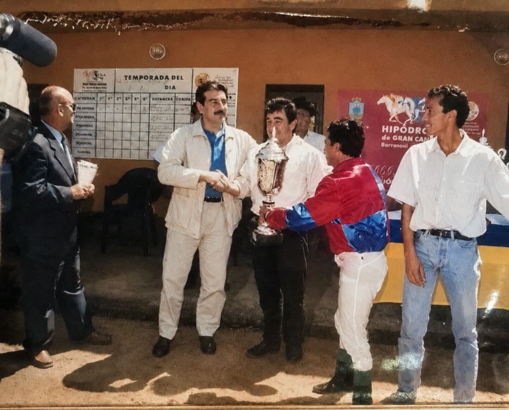 Entrega del Premio Gobierno de Canarias en el hipódromo: un hombre estrecha la mano al jinete mientras otro sostiene la copa