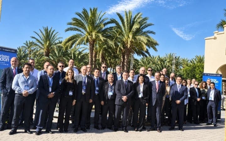 Fotografía de grupo de los asistentes a un curso y conferencia para empresarios en Barcelona, al aire libre entre palmeras y junto a los carteles del encuentro